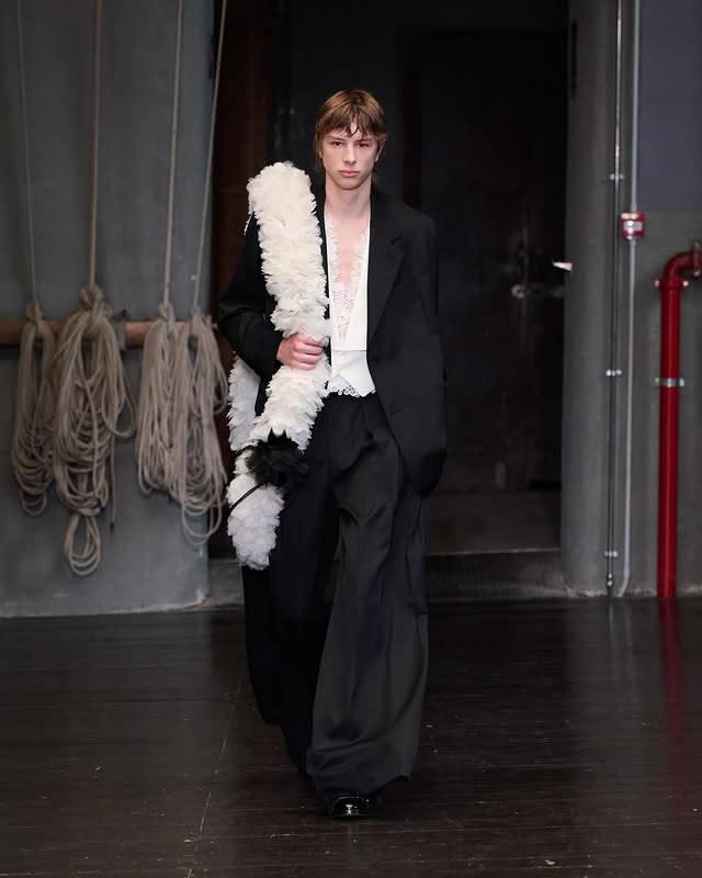 Simone Rocha menswear ss27 - Look 2 PAVLO A suit. Single-breasted backless jacket with apron tie, and wide-legged trousers with deep kilt pleats, in Venetian wool